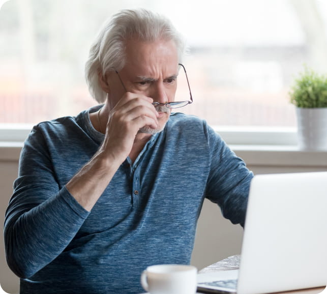 Older adult rubbing their eyes while using a laptop, illustrating blurred or fluctuating vision.