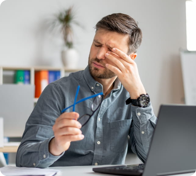 Person at a laptop holding their glasses and rubbing their eyes, illustrating eye discomfort